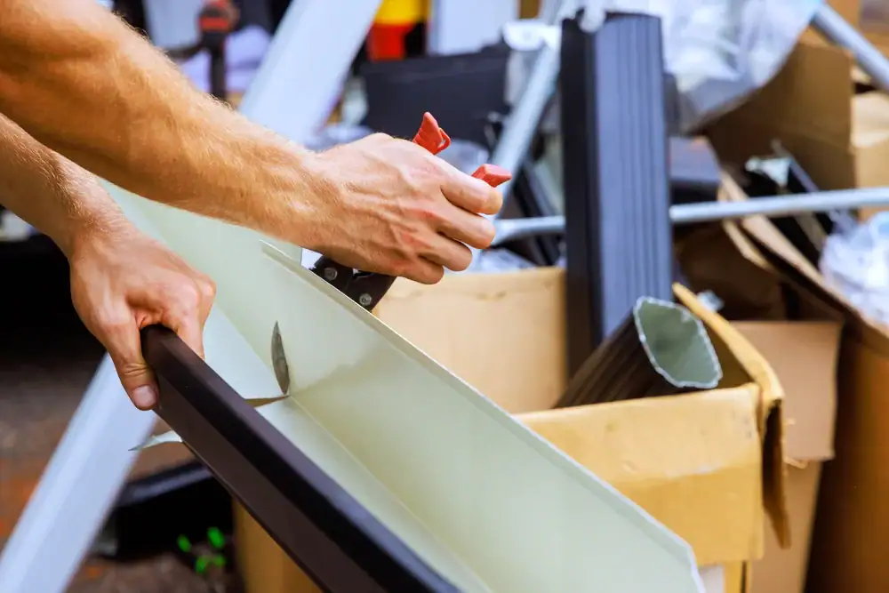 Close-up of a person’s hands using a tool to cut white metal amidst construction materials and cardboard boxes, capturing a busy home construction scene in Suffolk County, NY.
