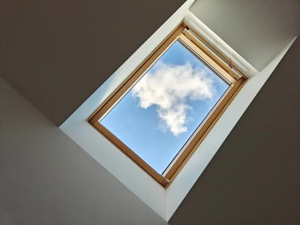 A skylight window set in a white ceiling shows a blue sky with a single fluffy white cloud, adding natural light and charm—perfect for modern home construction in Suffolk County, NY.