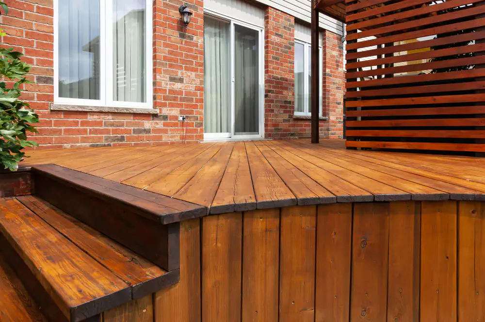 A close-up view of a wooden deck with steps and a privacy screen, attached to a red brick house with sliding glass doors—an example of quality home construction in Suffolk County, NY.