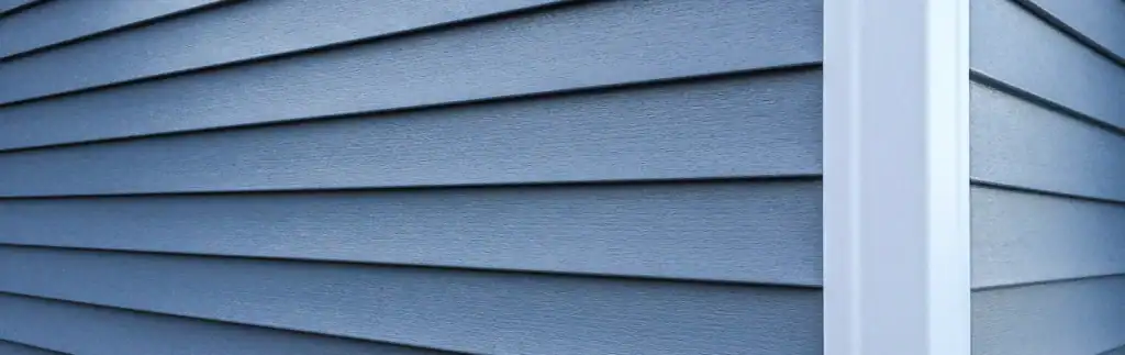 Expert vinyl siding repair on a blue house exterior by Home Team Construction.