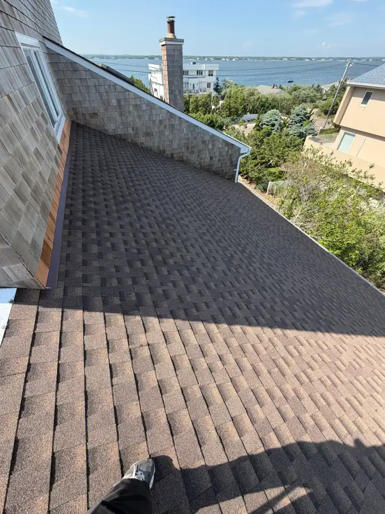 Newly installed asphalt shingle roof with scenic water view in background.