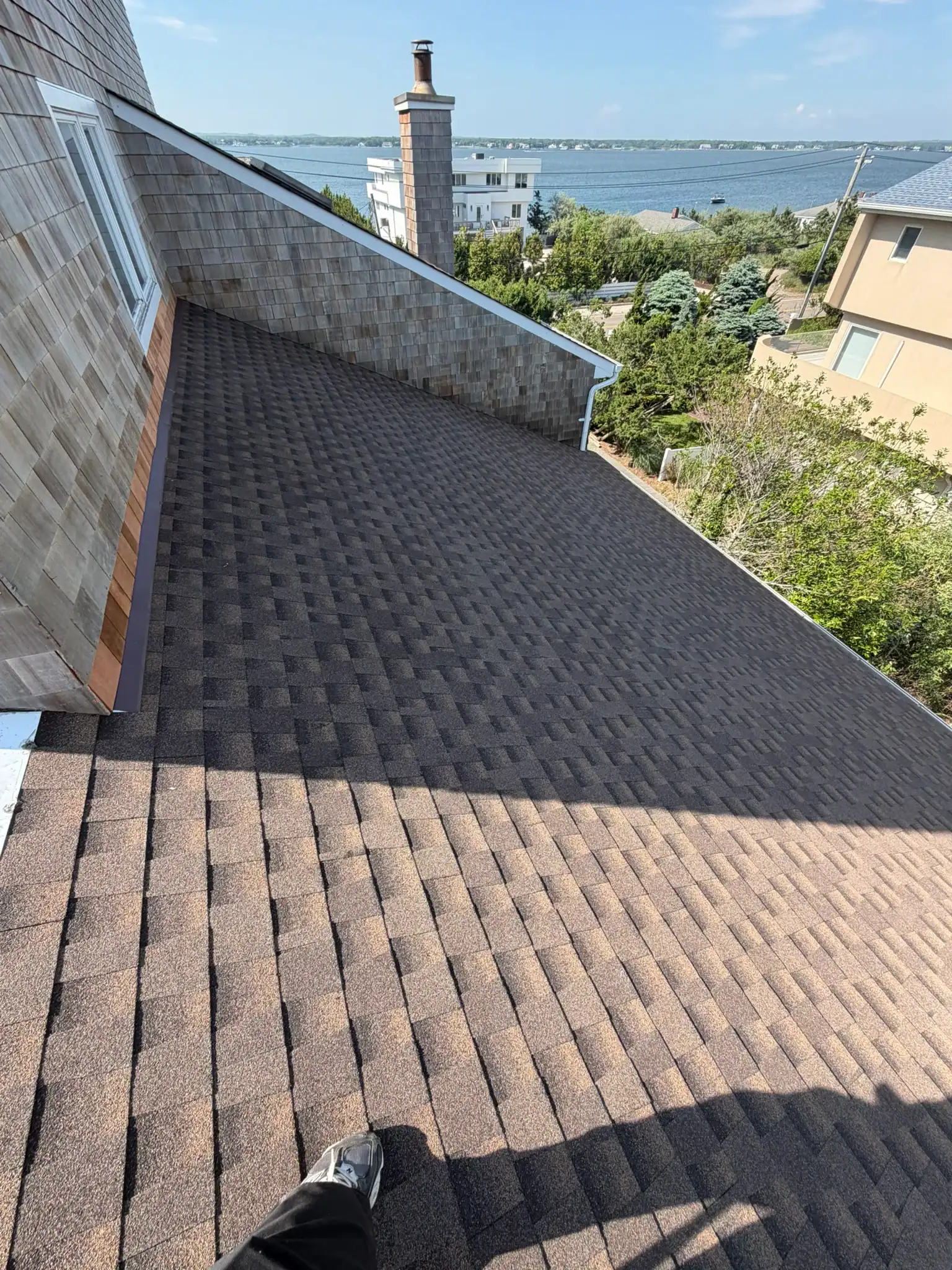 Newly installed asphalt shingle roof with scenic water view in background.