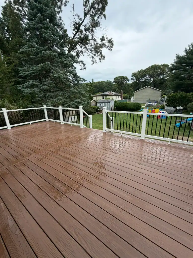 Newly built wooden deck with white railing in a backyard after rain.