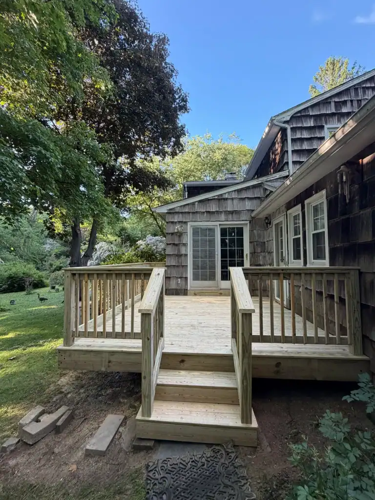 New wooden deck with stairs and railing attached to a house in a lush backyard.