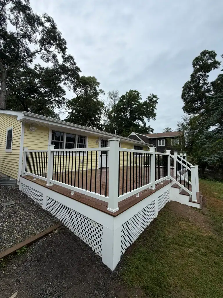 Newly built wooden deck with white railing in backyard of house.
