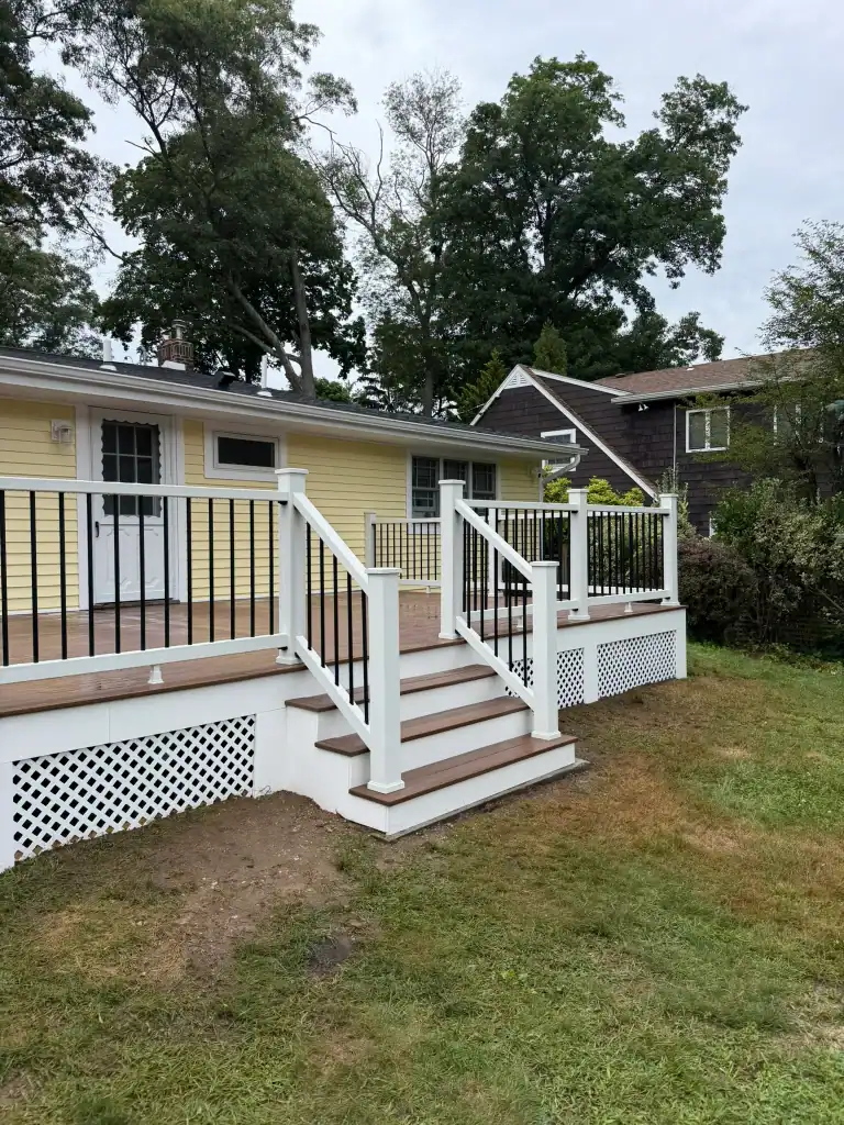 Newly built wooden deck with white railing in backyard of yellow house.