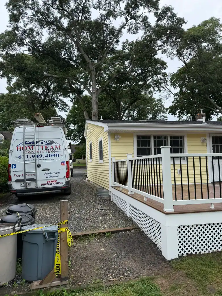 Yellow house with a deck and a construction van parked nearby.