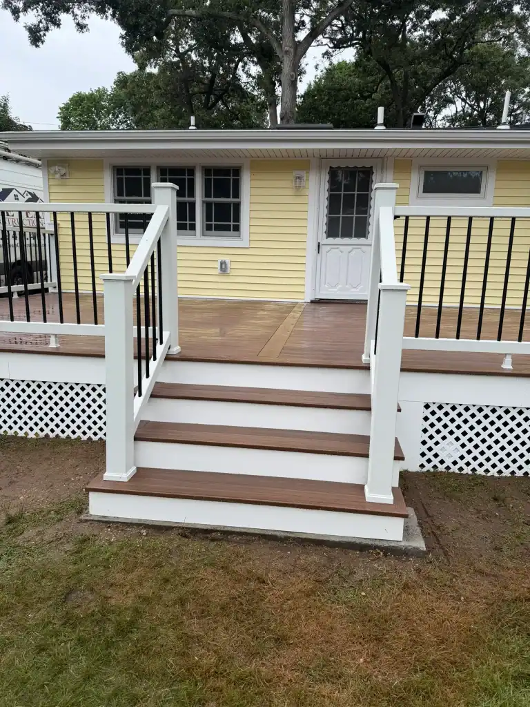 Newly built yellow house with a wooden deck and black railing.