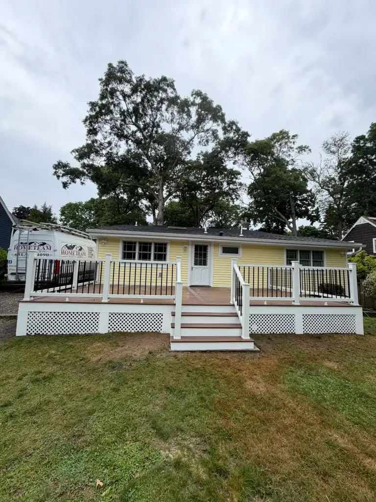 Yellow house with a large wooden deck and white railing in a suburban yard.